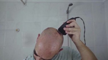 Evdeki bir adam saçını banyo aynasının önünde elektrikli jiletle tıraş ederek bitiriyor..