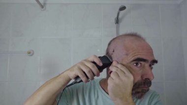 Bakım rutiniyle meşgul olan bir adamın yakın plan çekimi, evde kafasını tıraş makinesiyle traş etmesi..