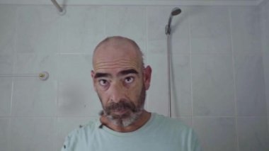 Evde bir adam tıraş makinesi kullanırken banyodaki aynaya dikkatlice bakarak kafasını tıraş ediyor..