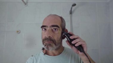 Sahne, iç mekanda kafasını tıraş makinesiyle dikkatlice tıraş eden bir adamı gösteriyor..