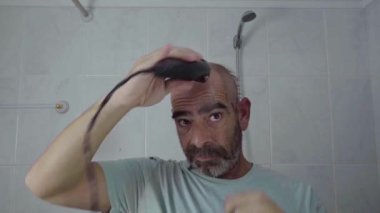 Bir adam elektrikli traş makinesi kullanarak evde saç kesimi yapıyor, kendi kendini yetiştirme alışkanlıklarını gösteriyor..