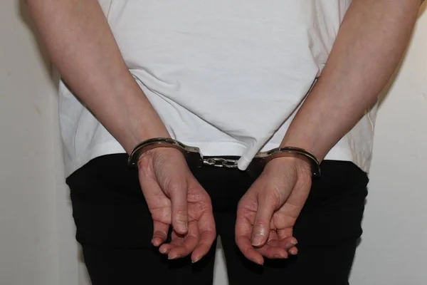 A female who has been arrested stands with her hands in handcuffs behind her back. The prisoner is waiting to be transported to jail in a police vehicle.