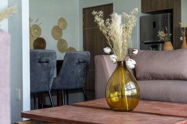 Kahverengi arka planı olan cam bir vazoda modern kurumuş çiçek aranjmanı. Boho tarzı, sıcak bir akşam. Kafe, iç mekan. Menü için kopyalama alanı olan arkaplan, davet kartı tasarımı