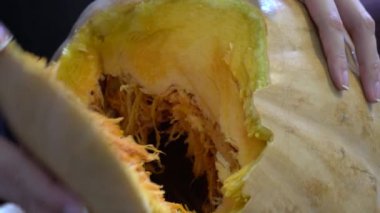 Cadılar Bayramı partisi için büyük turuncu balkabağı oyan dişi, evdeki ahşap masada otururken, şaka mı şeker mi havasında olmak için bıçağıyla balkabağı üzerinde korkunç bir yüz ifadesi yapıyor.