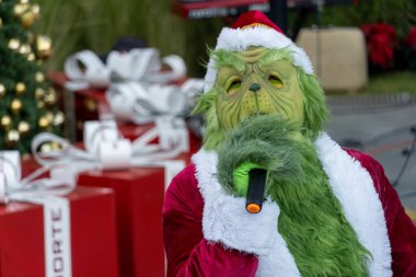 Büyük hediyelerle bir Noel ağacının arkasında şarkı söyleyip dans eden Grinch, Meksika Latin Amerika