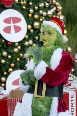 Büyük hediyelerle bir Noel ağacının arkasında şarkı söyleyip dans eden Grinch, Meksika Latin Amerika