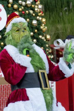 Büyük hediyelerle bir Noel ağacının arkasında şarkı söyleyip dans eden Grinch, Meksika Latin Amerika