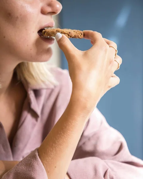 young latin woman eating cookie blue background, enjoying natural light
