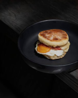 Kalın ev yapımı ekmekli yumurtalı sandviç, domuz pastırması, siyah seramik tabakta tuzlu yiyecek.