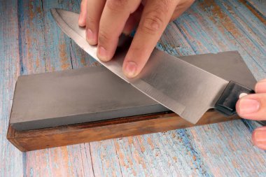 hand of a man sharpening a knife on a faded wooden table
