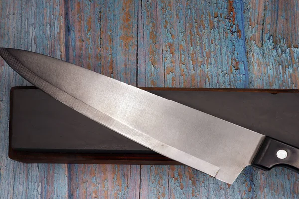 steel knife resting on a sharpening stone with a rustic wooden background
