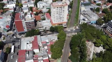 Güneşli bir günde Adrogue demiryolu ve tren istasyonunda ağaçlar ve binalarla kesişen katın havadan görüntüsü.