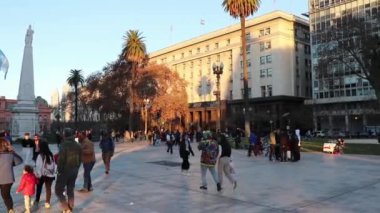 Buenos Aires Plaza de Mayo 'da gün batımı ve şehirde dolaşan turistlerin uzun gölgeleri.