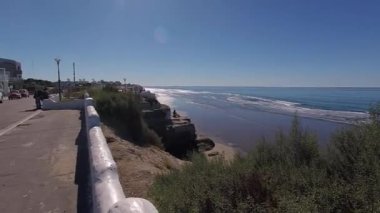 Güneşli bir yaz gününde, Las Grutas, Rio Negro, Arjantin 'deki bir sahil caddesinin açık mavi gökyüzü, yumuşak dalgalar, kayalıklar ve deniz manzaralı evleri..