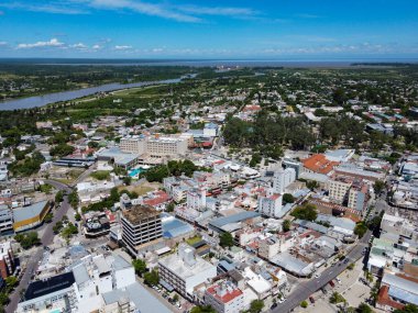 Termas de Rio Hondo 'nun açık bir gökyüzü altındaki panoramik görüntüsü, şehir siluetini, engin su deposunu, dingin gölü ve MotoGP pistindeki heyecan vaadini gösteriyor. Termal refah ve motor coşkusu için bir hedef, sıcaklığın davet ettiği yer.