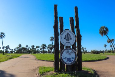 El Palmar Ulusal Parkı 'na giriş işareti, beyaz arka planda siyah harflerle' PARQUE NACIONAL EL PALMAR 'yazılı. Açık mavi gökyüzü ve çevreleyen bitki örtüsü