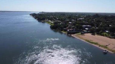 Güneşli bir günde Parana Nehri 'nden plajlara ve Paso de la Patria, Corrientes şehrine insansız hava aracı atışı. Ağaçlarla çevrili turizm ve balıkçılık merkezi