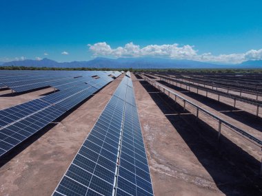 Güneş panellerinin geniş alanlarını aydınlatan güneşli gökyüzünün altında, uzakta And Dağlarının görkemli varlığı Arjantin 'in alternatif enerjilere giden yolunun bir sembolü olarak duruyor..