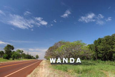 Wanda, Misiones, Arjantin 'e hoş geldiniz işareti. Yarı değerli taşları, jeoidleri ve madencilik faaliyetleri için sembolik bir şehir. Bereketli bitki örtüsü girişi aydınlık güneşin altında hazinelerinin keşfedilmesine yol açan bir yol ile donatıyor.