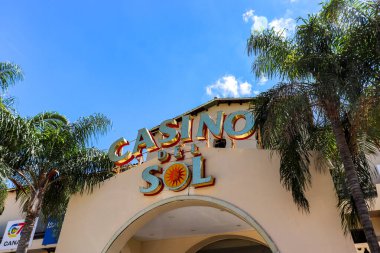 Termas de Rio Hondo 'daki Casino del Sol' un giriş kapısı. Palmiye ağaçları ve mavi gökyüzünün altında kendine özgü bir işareti var. Çevreleyen bitki örtüsü sahneyi tamamlıyor.