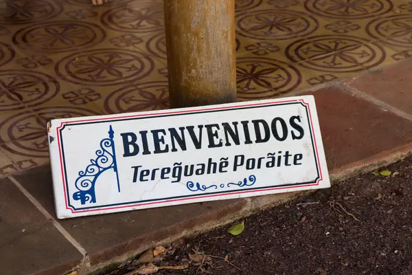 Yere dayanan eski bir metal tabela, klasik tipografi ve büyük harflerle İspanyolca ve Guarani dillerinde hoş karşılanan kelimeler sergiliyor. Corrientes Capital, Arjantin 'de çekildi
