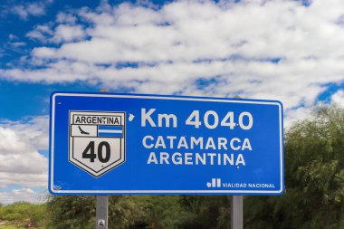 Km 4040 ve Catamarca Arjantin 'i gösteren açık mavi bir Ulusal Otoyol tabelası 40. Otoyol' da bulutlarla dolu canlı bir gökyüzünün altında kilit bilgilere odaklanıyor..