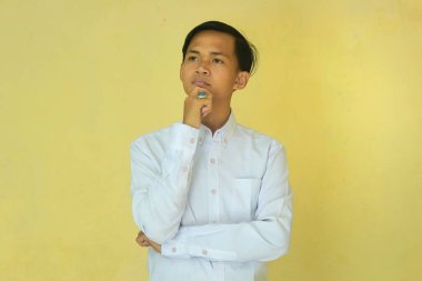 Beyazlı bir adam eli çenesinde durup düşünceli bir ifade sergiliyordu. Kafası karışmış bir adam sarı bir arka grupla izole edilmiş.