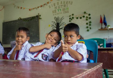 Simalungun Endonezya, 16 Ocak 2024-3 Endonezyalı ilkokul çocuğu okul bankında mutlu bir şekilde gülümsüyor.