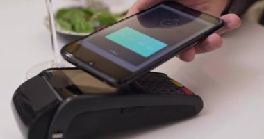 Yakın çekim müşteri eli kablosuz ödeme NFC teknolojisi yapmak için akıllı telefon kullanır. 4k 'lık kontaksız salgın hastalık konseptini kapatın.
