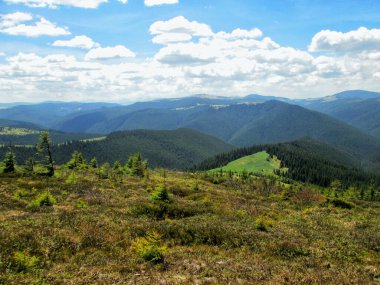 Baharda geniş bir dağ manzarası yemyeşil vadiler ve dağınık bulutlarla