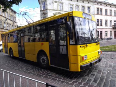 Eski sarı bir troleybüs öğle yemeği molasında park etmiş, tarihi şehir mimarisinin arka planına karşı.