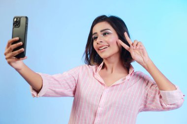 Image of beautiful Hispanic girl taking her selfie or talking on a video call isolated over gradient blue background