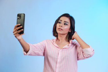 Image of beautiful Hispanic girl taking her selfie or talking on a video call isolated over gradient blue background