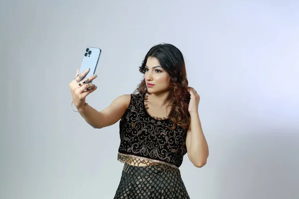 年轻而美丽的印度裔巴基斯坦德西族女孩穿着德西族服装 通过手机前视镜来调整头发和检查自己 — 图库照片