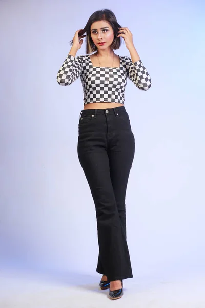 Young stylish bold fit and slim girl walking casually, looking in camera isolated on a studio background. The girl is wearing black and white trendy shirt with black bell bottom pants and high heels