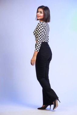 Young attractive Slim fit girl posing casually, looking in camera isolated on a studio background. The girl is wearing black and white stylish shirt with black bell bottom pants and high heels