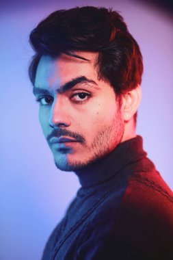 Neon light studio close-up portrait of serious man model wearing a turtle neck knitted sweater