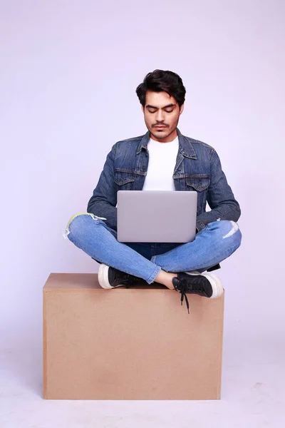 Casual Trendy Pakistani man sitting with laptop and busy working on a box