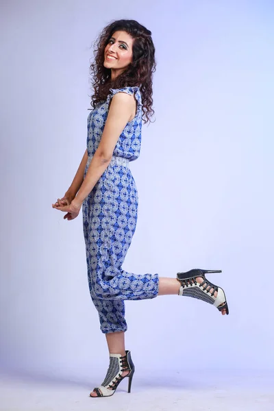 young Hispanic fashion girl with curly hair in a jumpsuit, Posing wuth one leg raised, High fashion concept. Isolated on a studio backround
