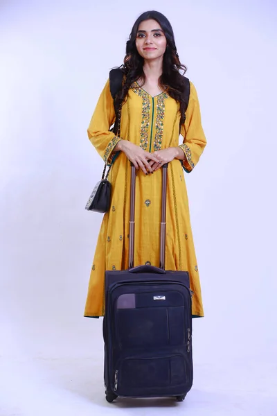 young Desi traveler with luggage, girl has a shoulder carry on bagack along with a trolly luggage bag, in a yellow Kurti