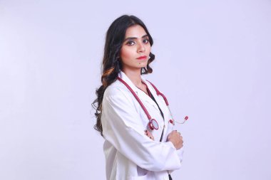 Young confident Pakistani Female doctor wearing a white doctor's coat and hanging stethoscope, Standing on with her arms folded looking in camera