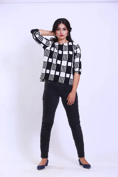 Young attractive fit woman posing casually, looking in camera isolated on a studio background. The girl is wearing black and white stylish shirt with black pants