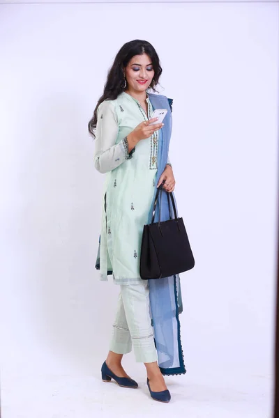 Beautiful Pakistani Woman in traditional embroidery shalwar kameez dress with dupatta. Walking holding a smartphone with a smile `Desi Fashion Concept