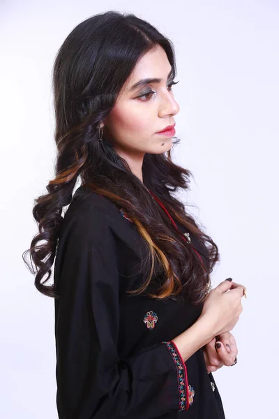 side profile portrait of a Pakistani girl, in a black dress, looking away from camera. Isolated over white background