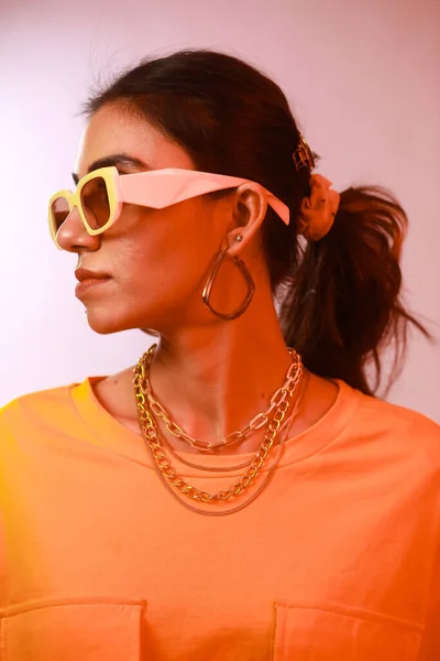 Neon Portrait of a fashionable trendy girl with sunglasses and gold chains, looking away from camera