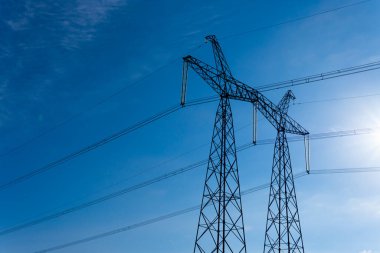 Mavi gökyüzüne karşı elektrik iletim hatları olan yüksek voltaj kulesi, düşük açılı görüş.