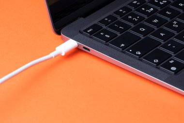Pil dizüstü bilgisayarı yükleniyor. Hızlı şarj için modern USB C portu. Dizüstü bilgisayara takılı beyaz kablo yakın çekim görüntüsü
