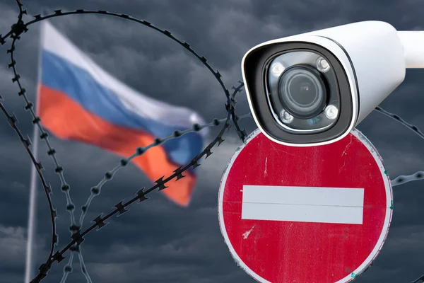 Barbed wire with a security camera on the background of the flag of Russia