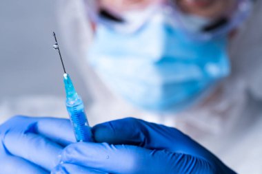 Close up man doctor holding syringe. Doctor in surgical mask and gloves preparing syringe for injection