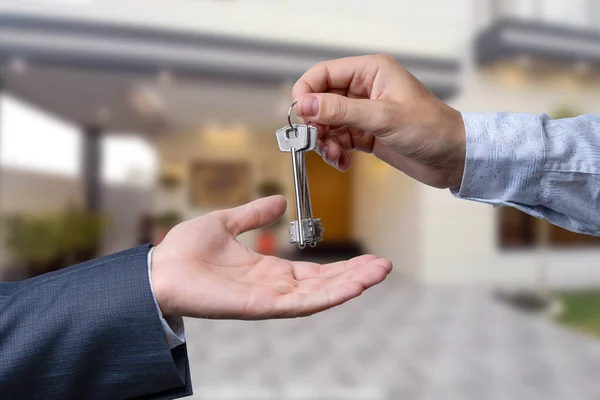 stock image A hand giving a key to another hand. House in the background